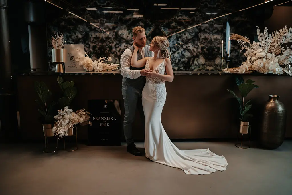 Brautpaar posiert zusammen vor dem Bartisch